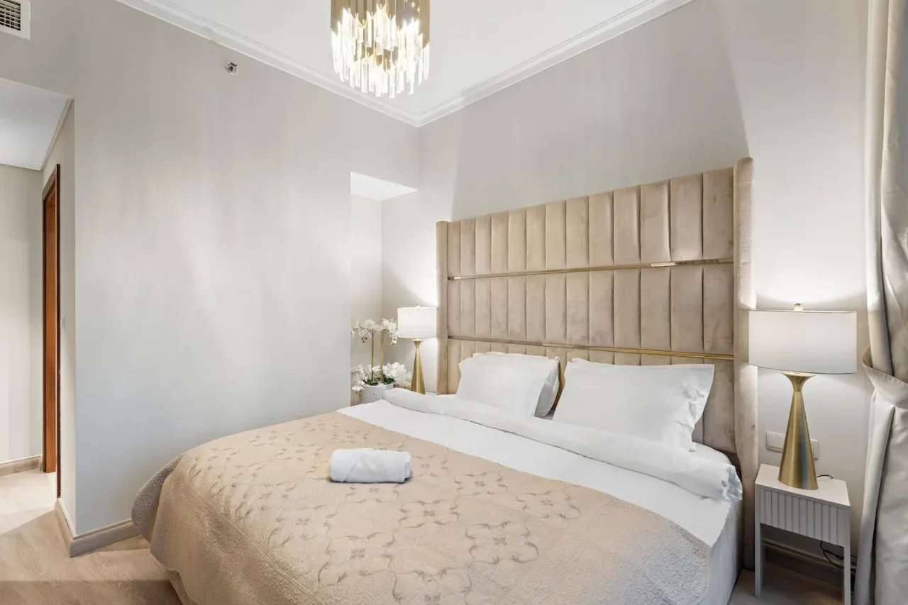 A bedroom with a large bed, bedside lamps, and a chandelier.