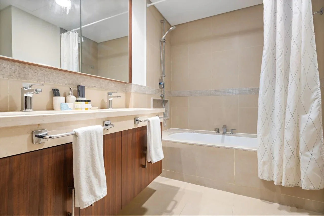 A bathroom with a long vanity, mirror, and bathtub behind a shower curtain.