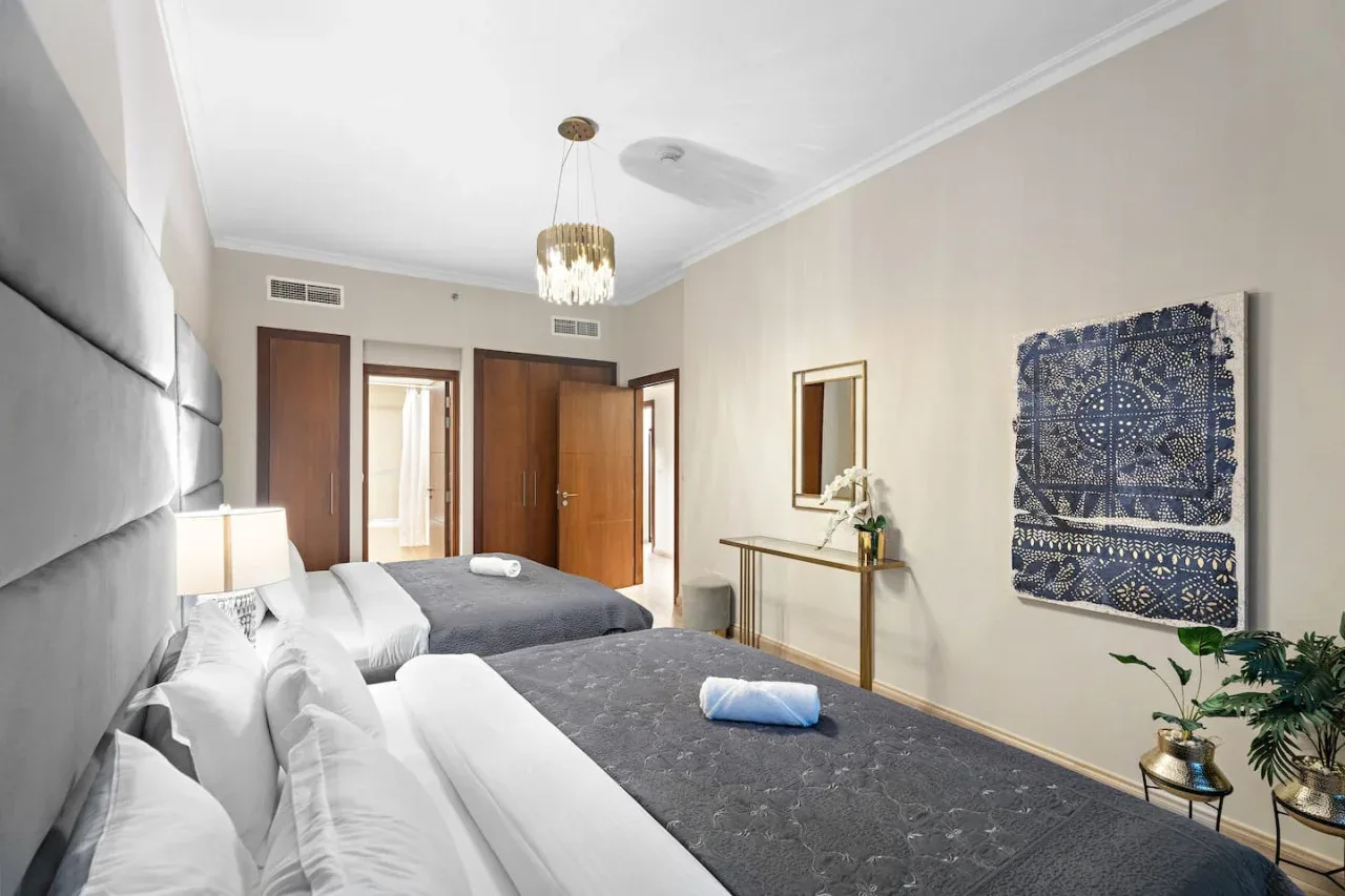 A bright bedroom with two beds and blue patterned wall art.