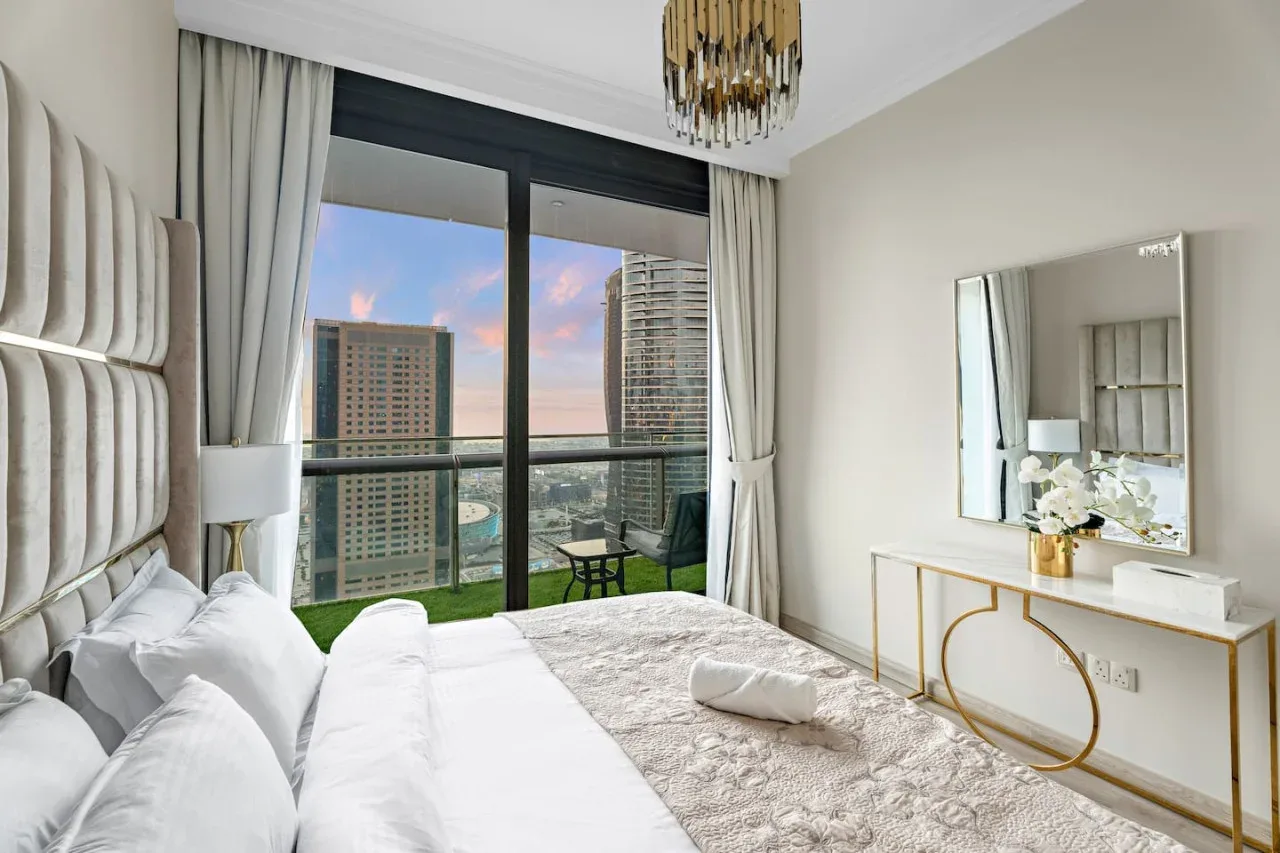 A bright bedroom with a large window overlooking nearby buildings.