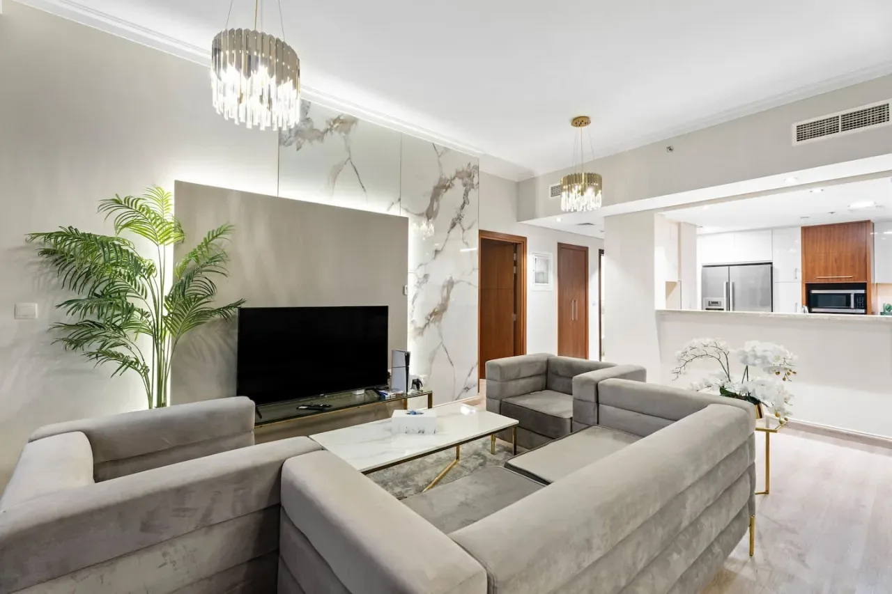 A bright living room with seating, a television, and an open kitchen.