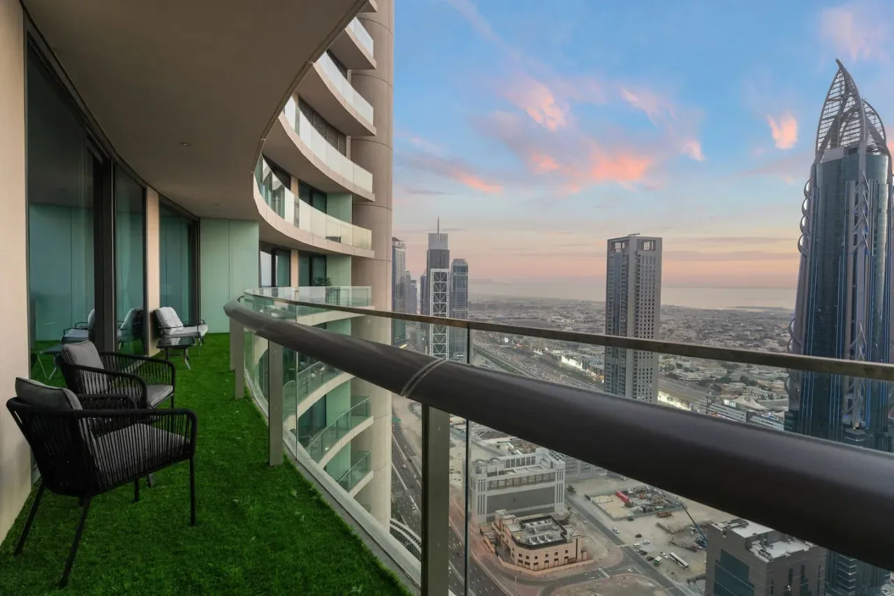 A curved balcony with seating overlooks a city skyline at sunset.
