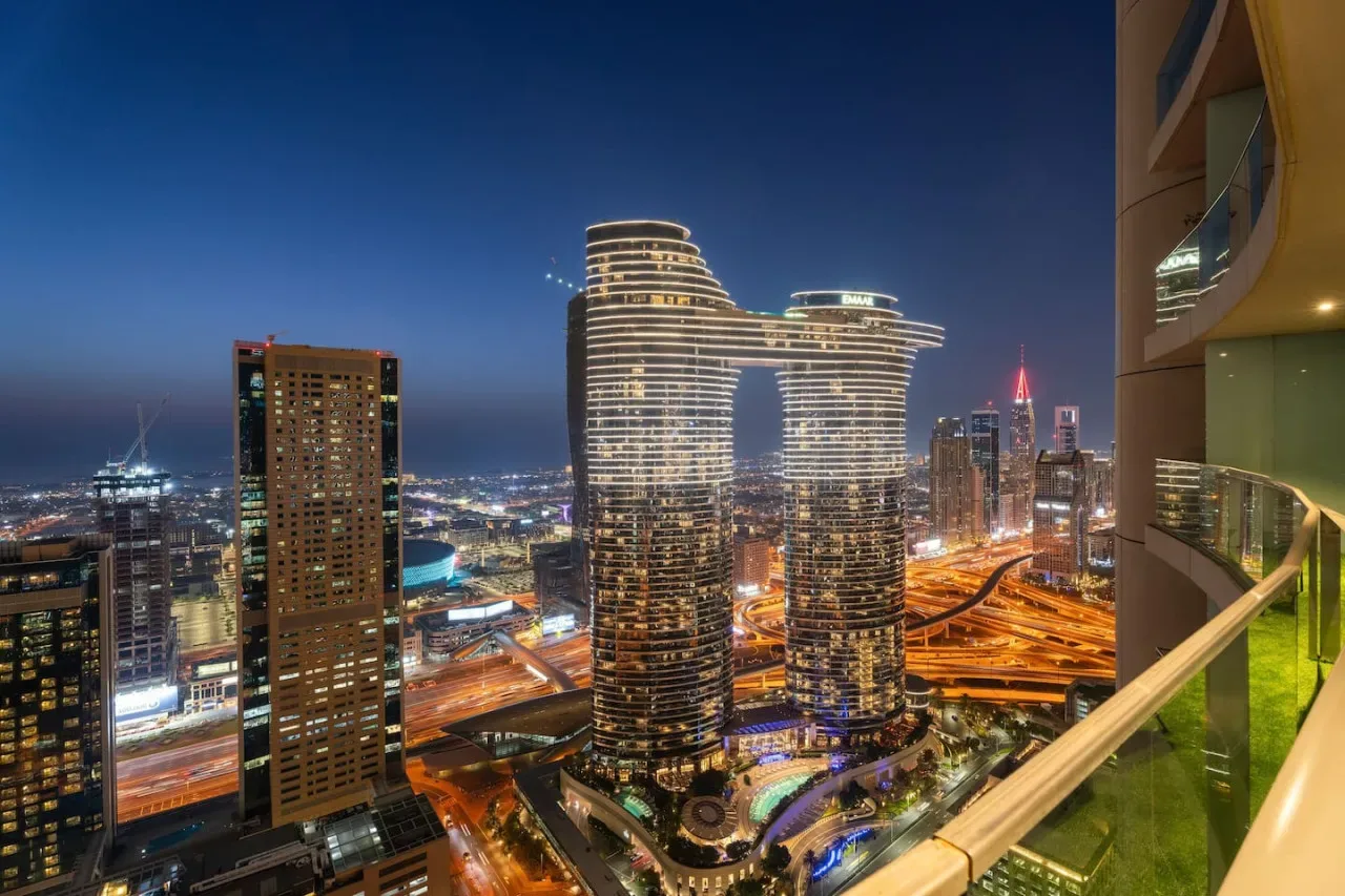 A nighttime city skyline seen from a balcony, with illuminated high-rise buildings.