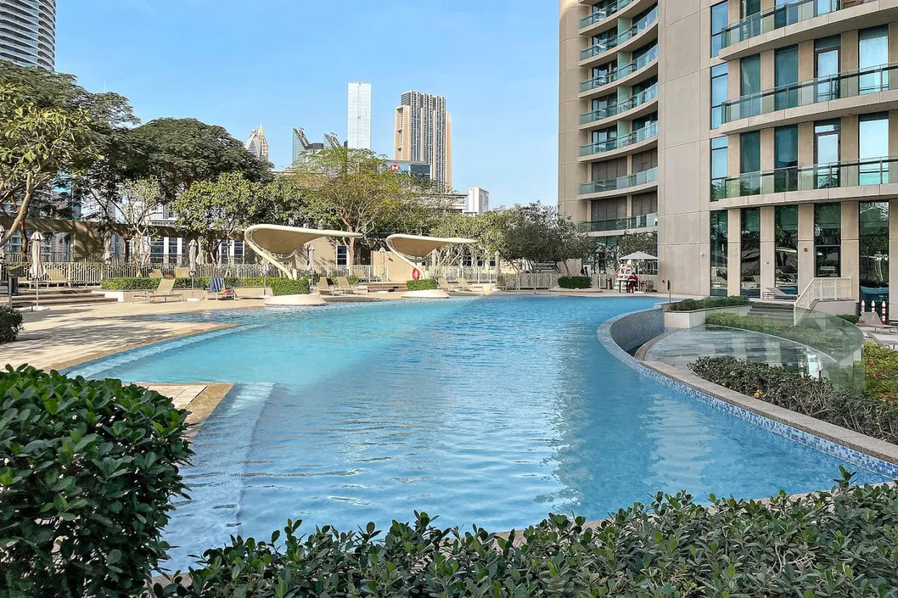 A swimming pool curves beside a landscaped courtyard and modern buildings.