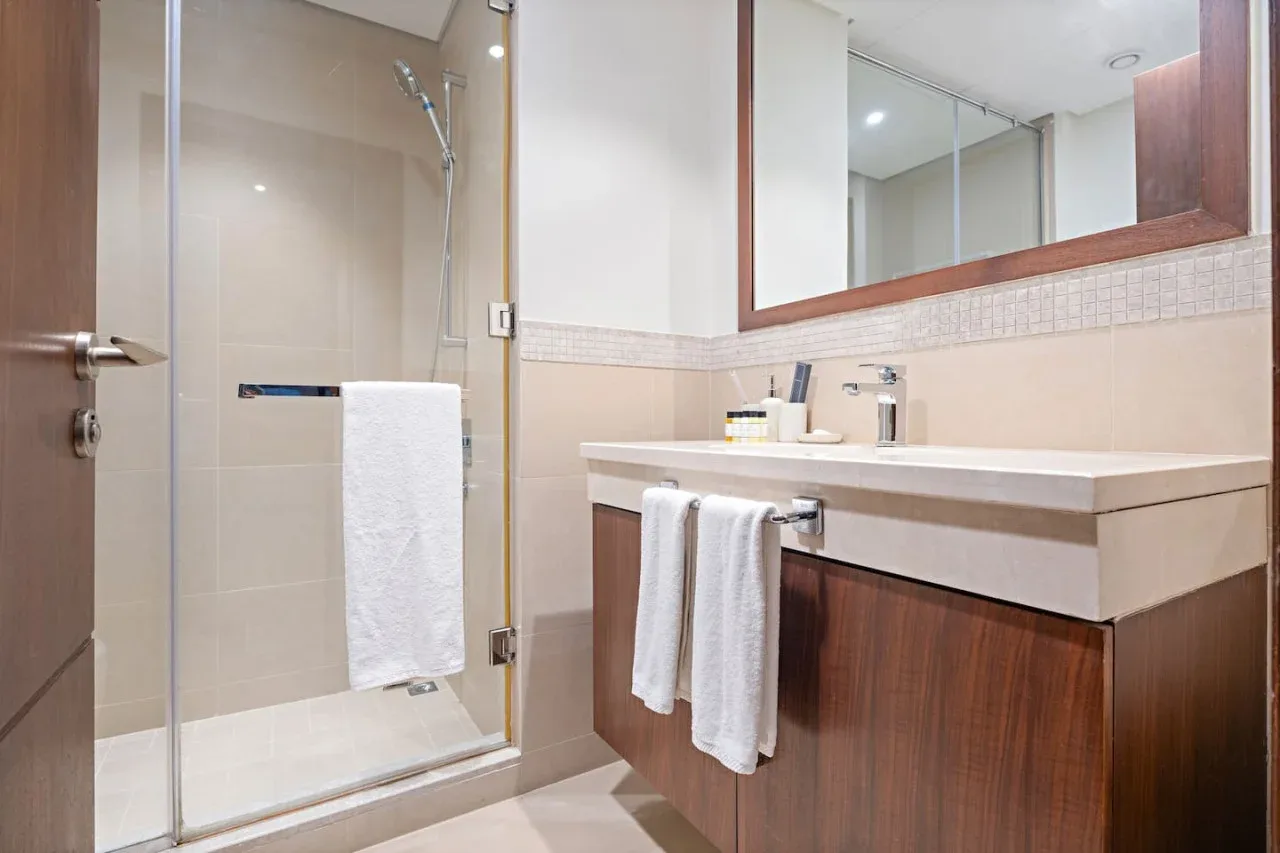 A bathroom with a glass shower and a vanity beneath a large mirror.