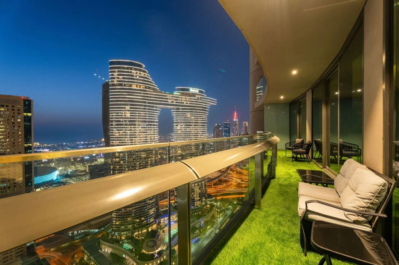 A balcony seating area overlooks illuminated city buildings at dusk.