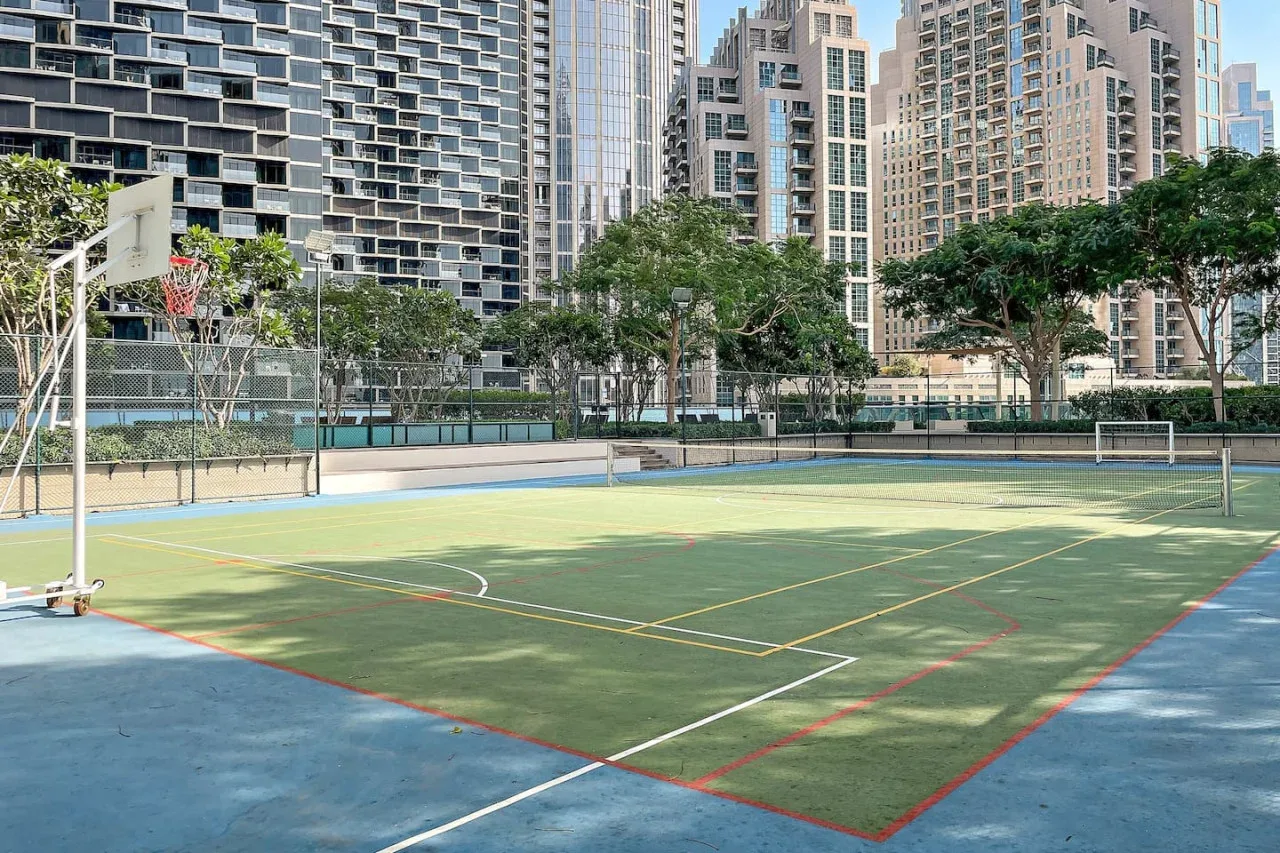 An outdoor sports court with a basketball hoop and tall buildings in the background.