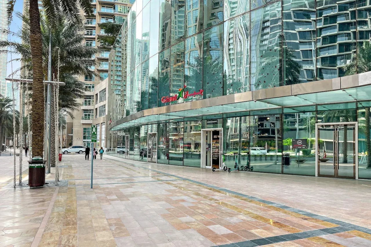 A glass-fronted building overlooks a wide paved pedestrian plaza.