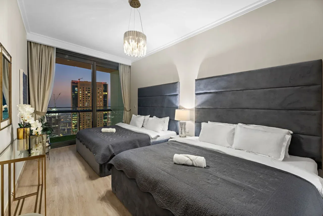 A bedroom with two beds and a large window overlooking nearby buildings.