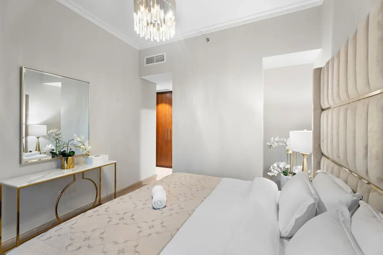 A bright bedroom with a bed and a mirrored console table.