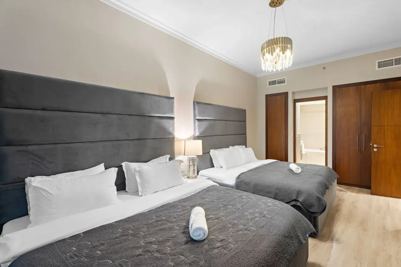 A bedroom with two beds, gray bedding, and dark upholstered headboards.