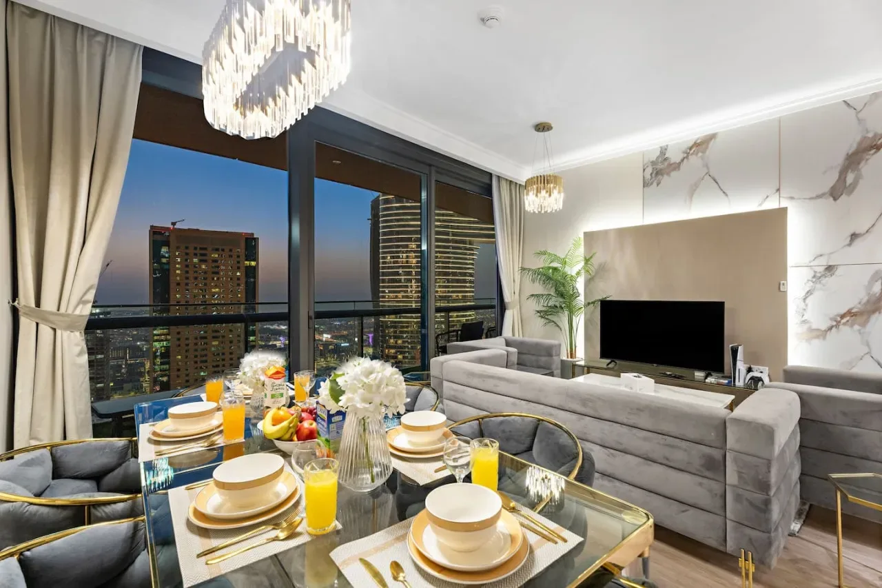 A modern living and dining area with a glass table and city views through large windows.