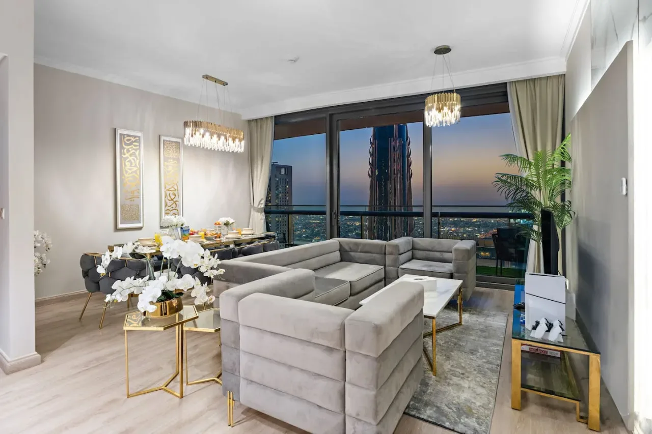 A modern living room with sectional seating, a dining area, and floor-to-ceiling windows.
