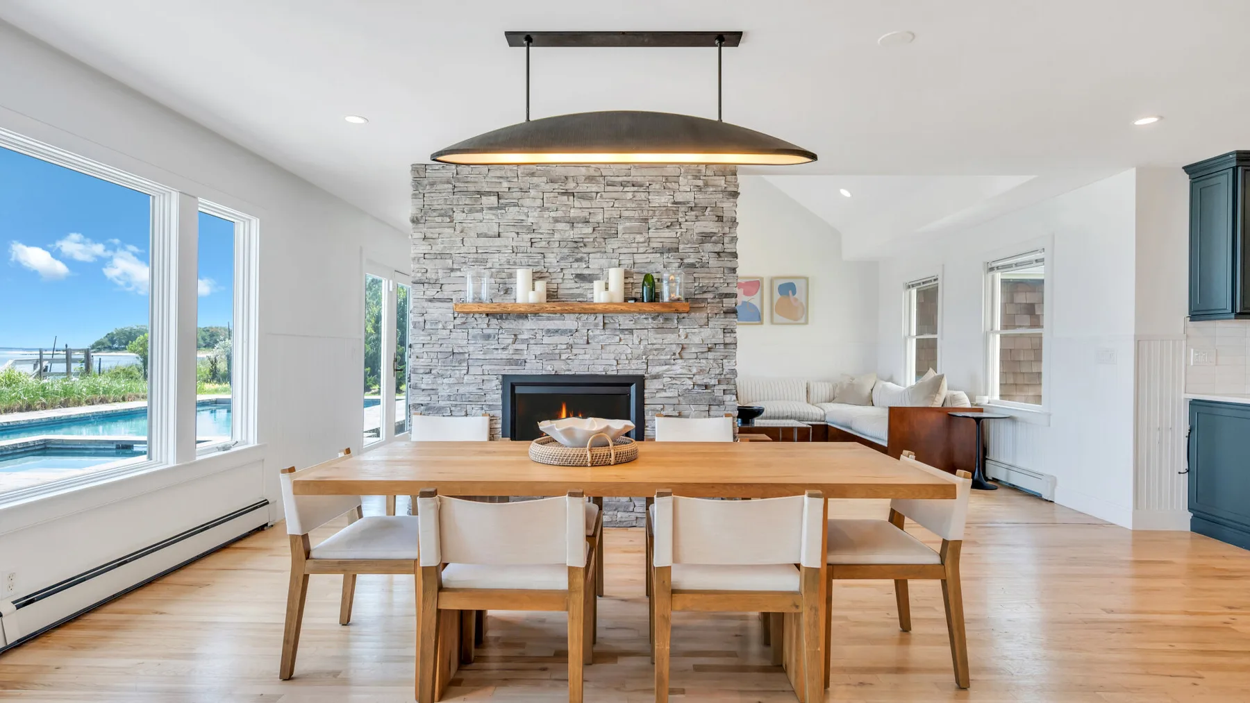 Un comedor y sala de estar diáfanos y luminosos, con chimenea de piedra y ventanales.