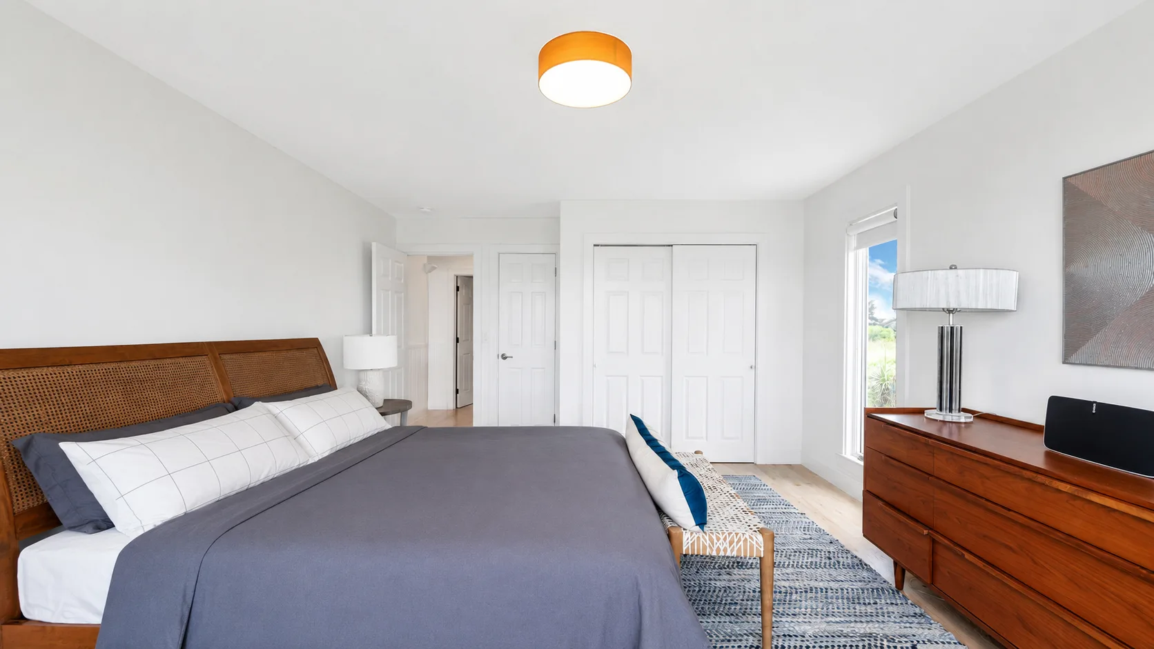 Un dormitorio luminoso con una cama tendida y una cómoda de madera.