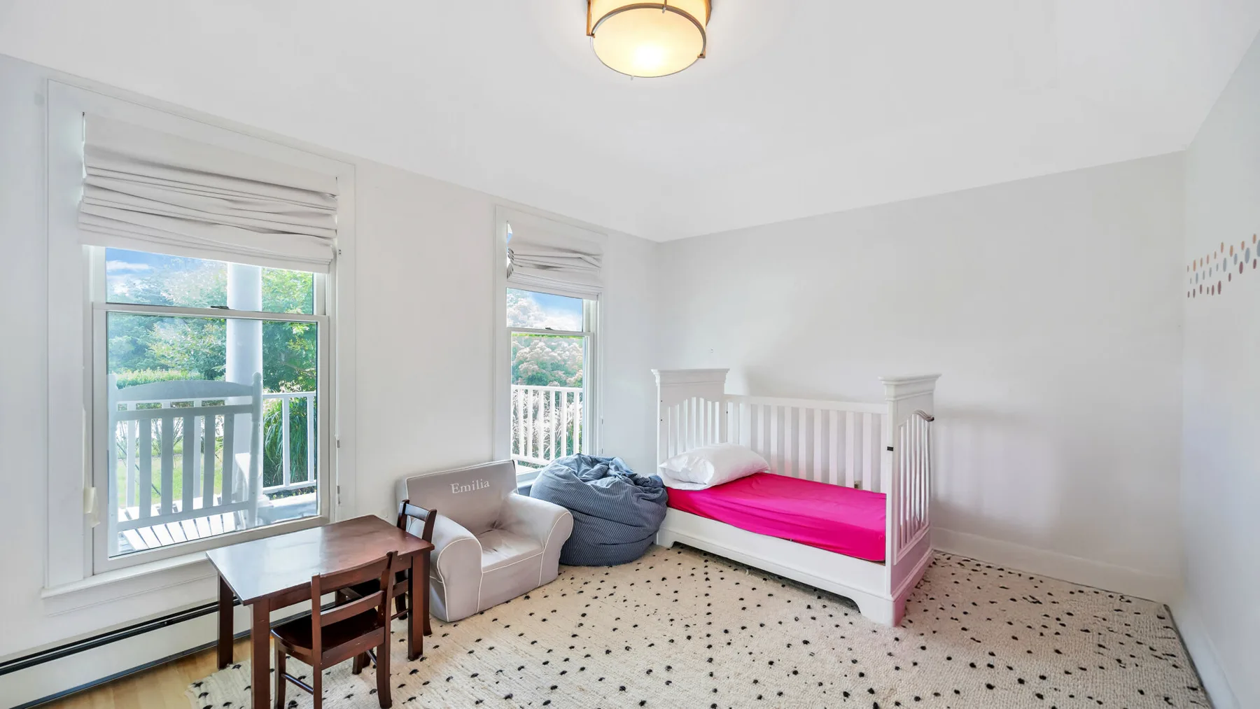 Un dormitorio luminoso con una cama rosa, un sillón y ventanas con vistas a la vegetación.