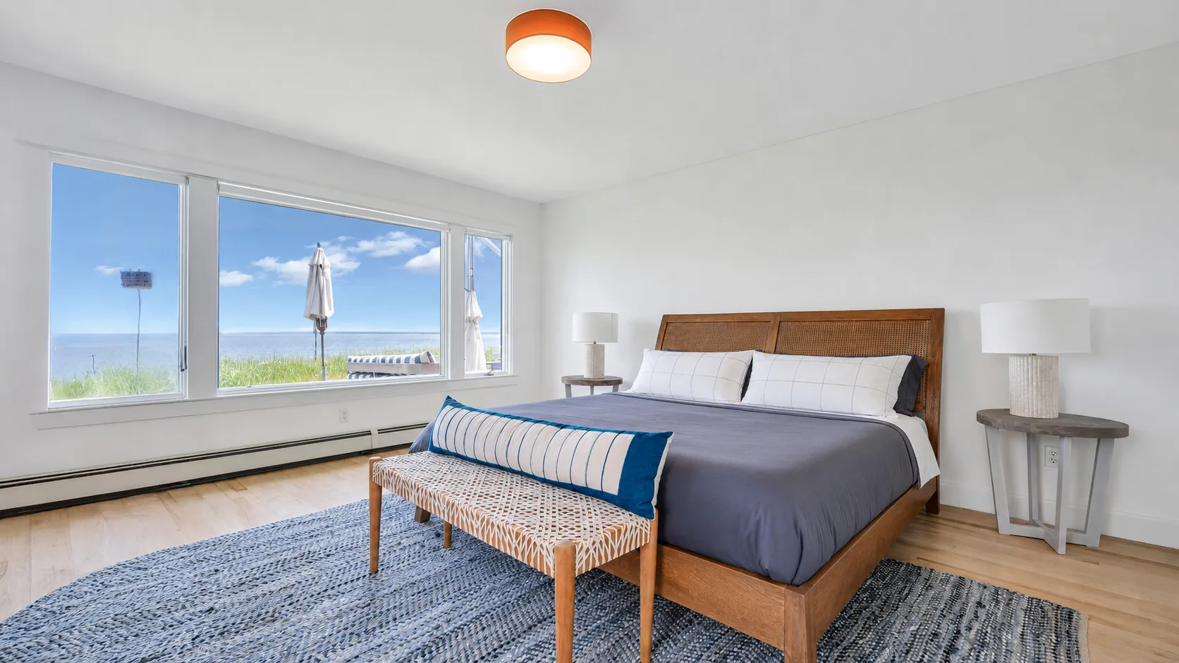 Dormitorio con una cama de madera, un banco y amplias ventanas con vista al agua.