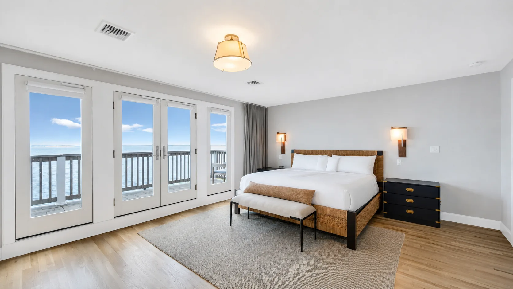 Dormitorio con una cama grande junto a ventanas con vistas al agua.
