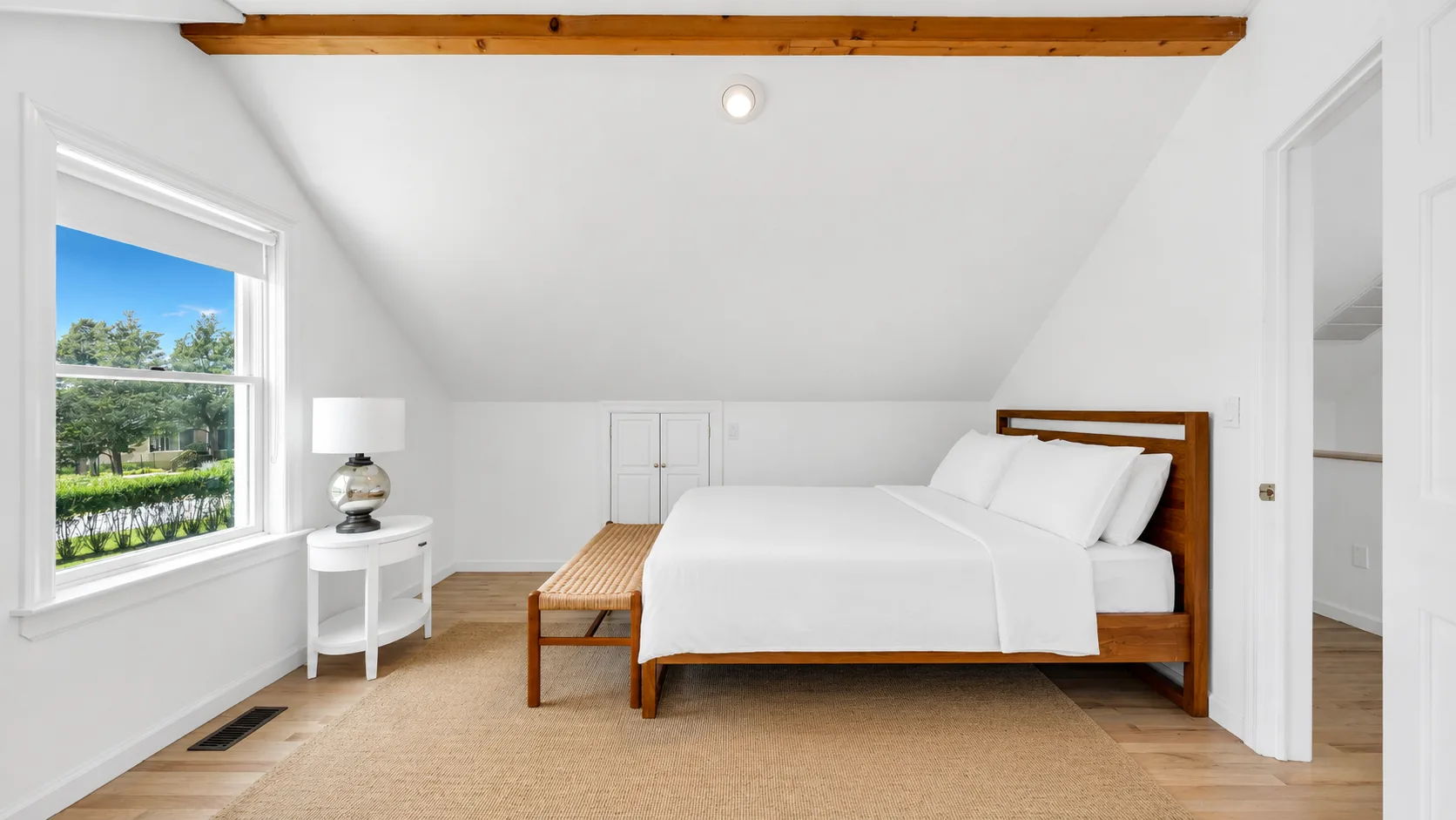 Un dormitorio luminoso con una cama tendida y una ventana grande.