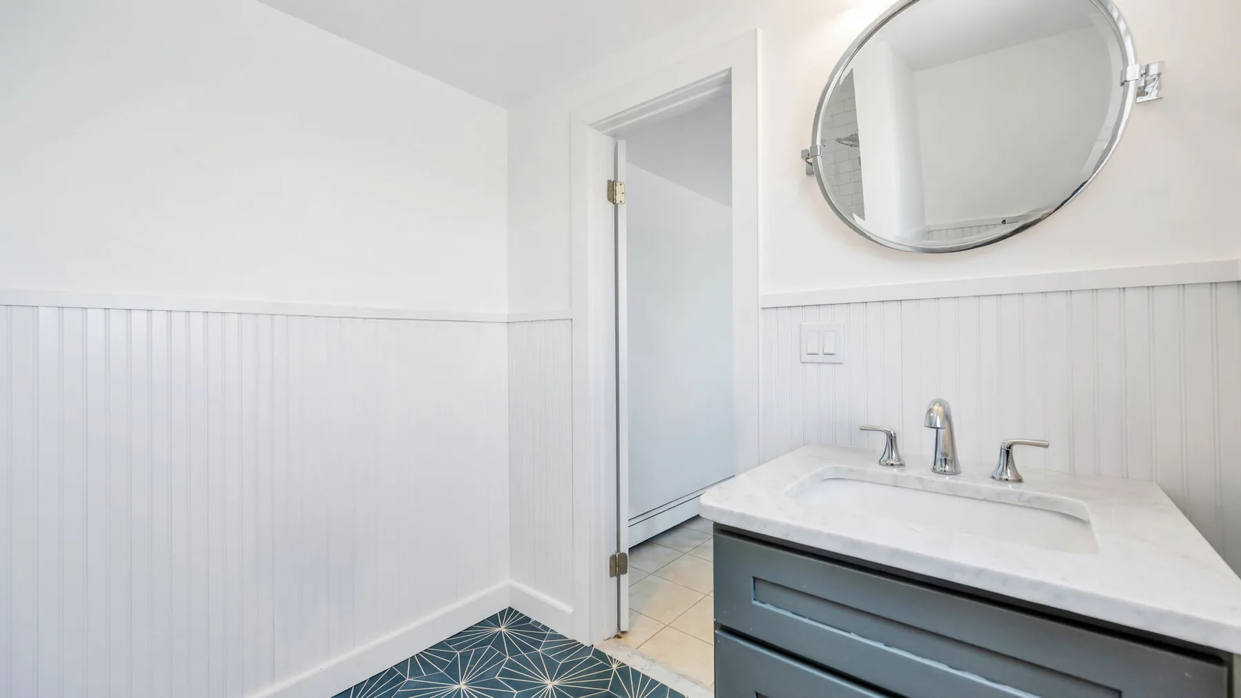 Un baño luminoso con lavabo, espejo ovalado y paredes blancas con paneles.