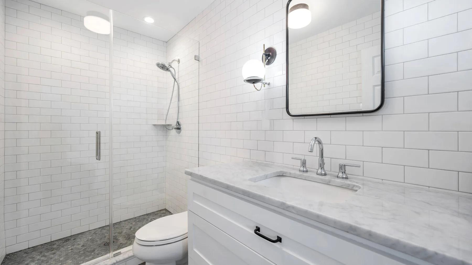 Un baño luminoso con azulejos, ducha de vidrio, inodoro y lavabo.