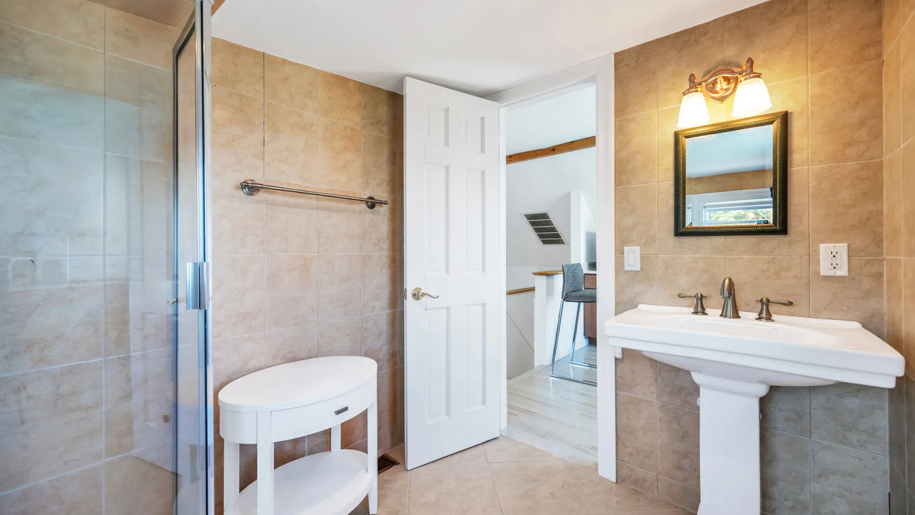 Un baño con azulejos, una ducha de vidrio, un lavabo y una puerta abierta.