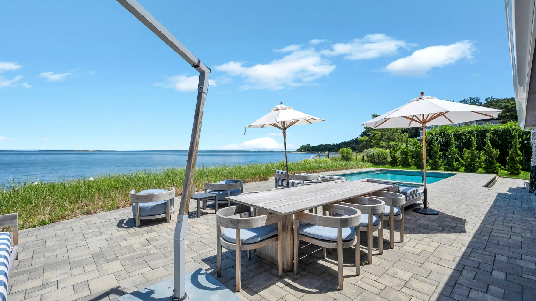 Una zona de comedor al aire libre pavimentada da a una piscina y al agua.