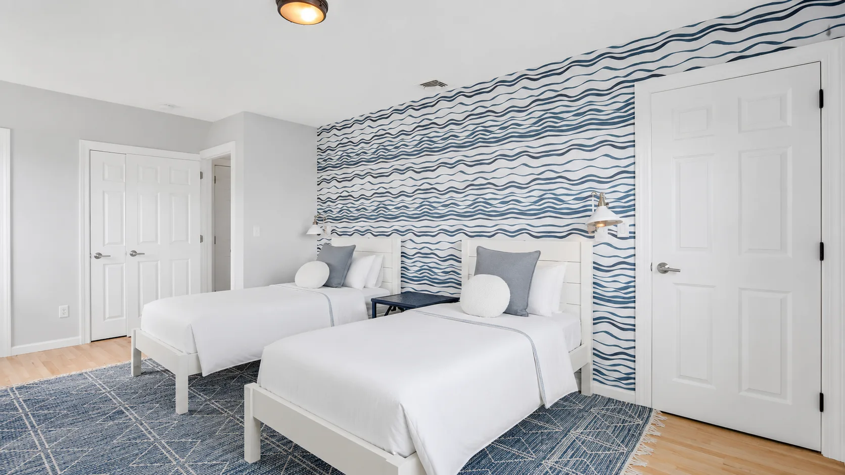 Un dormitorio luminoso con dos camas y una pared decorativa de ondas azules.