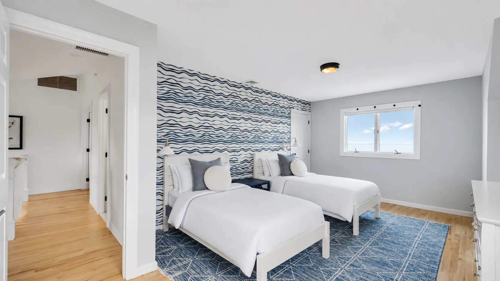 Un dormitorio luminoso con dos camas, papel tapiz estampado y una alfombra azul.