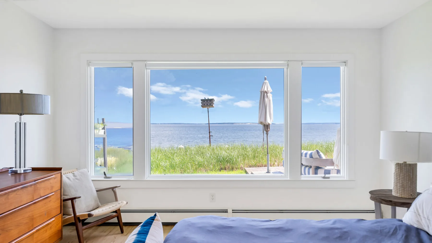 Un dormitorio luminoso con una cama y asientos junto a una amplia ventana con vistas al agua.