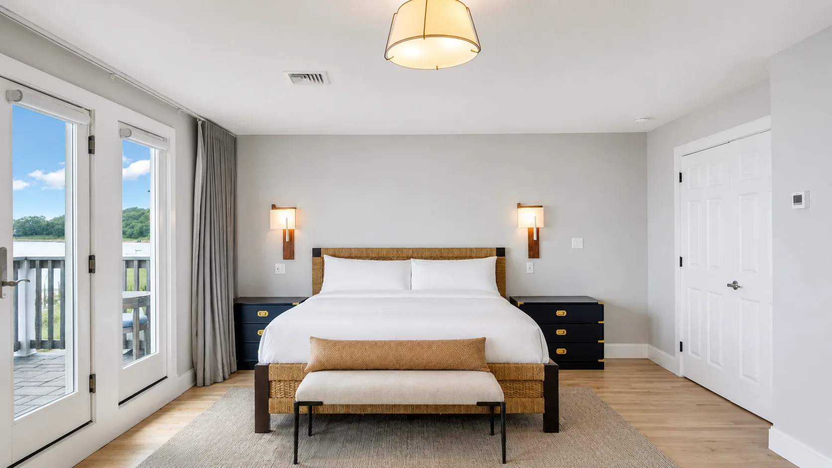 Un dormitorio luminoso con una cama bien hecha y puertas de vidrio que dan a un balcón.