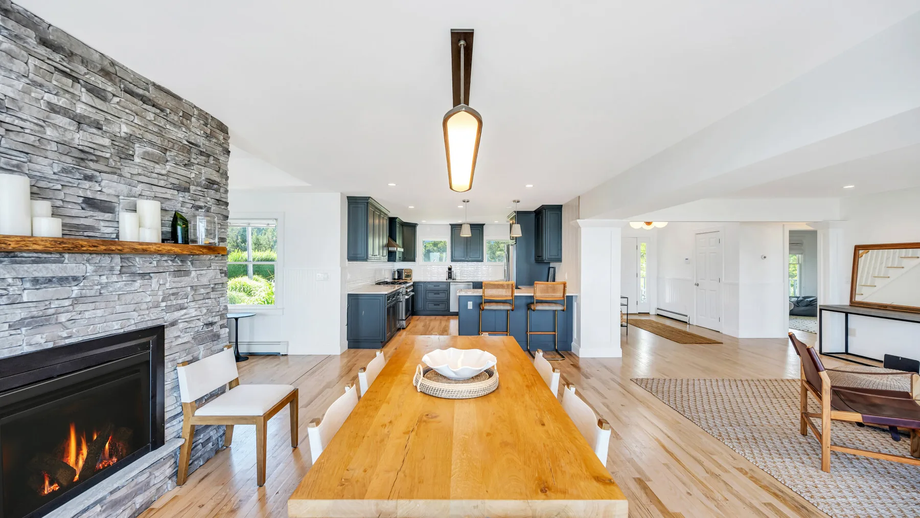 Una luminosa sala de estar y comedor de planta abierta, con una mesa larga de madera y una chimenea de piedra.
