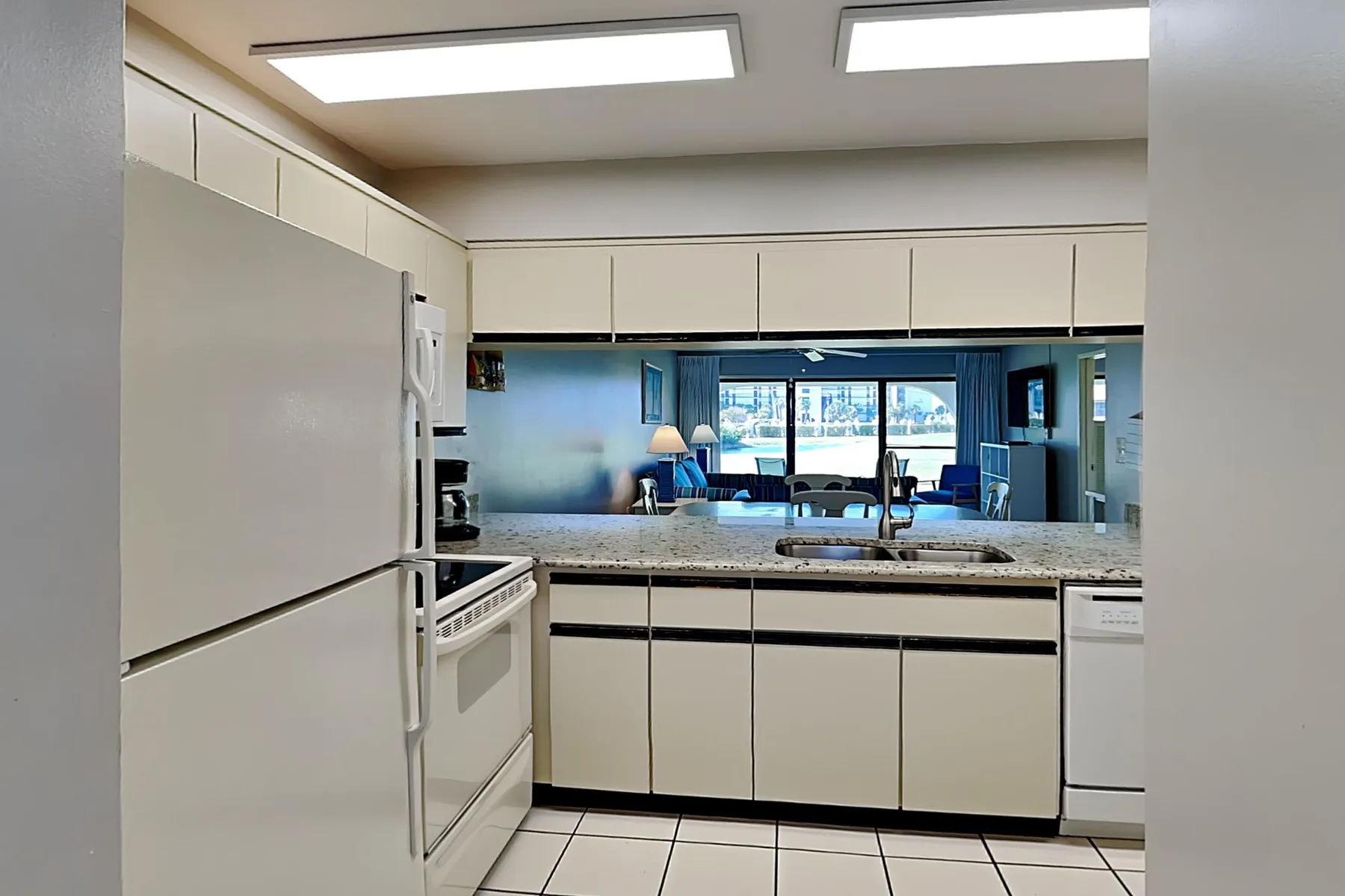 Una cocina luminosa con gabinetes blancos y una barra frente a una sala de estar.