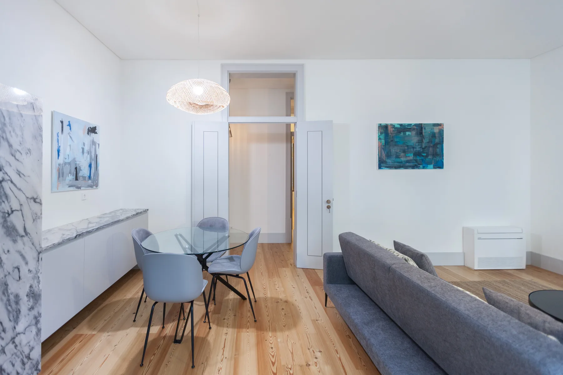 Una luminosa sala de estar y comedor con una mesa de vidrio y asientos grises.