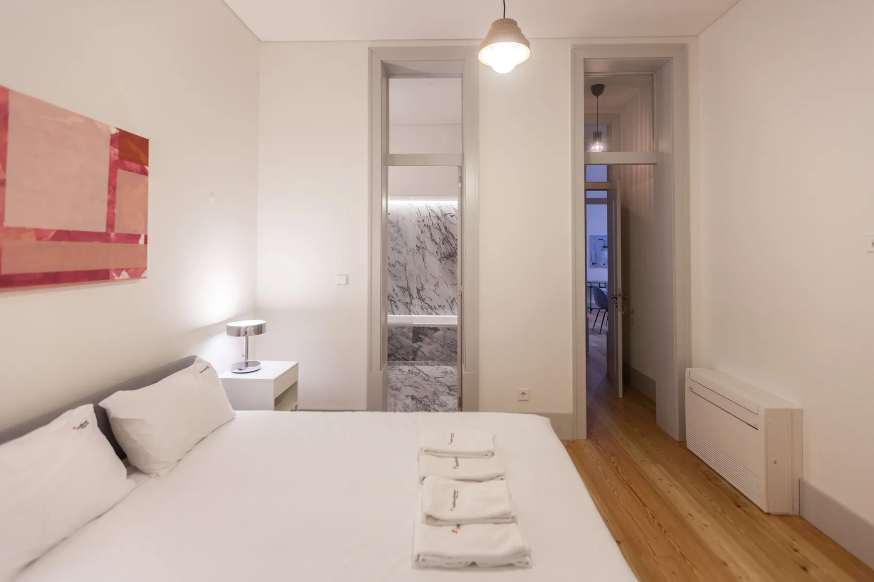 A bedroom with a neatly made bed and an open doorway to the bathroom.
