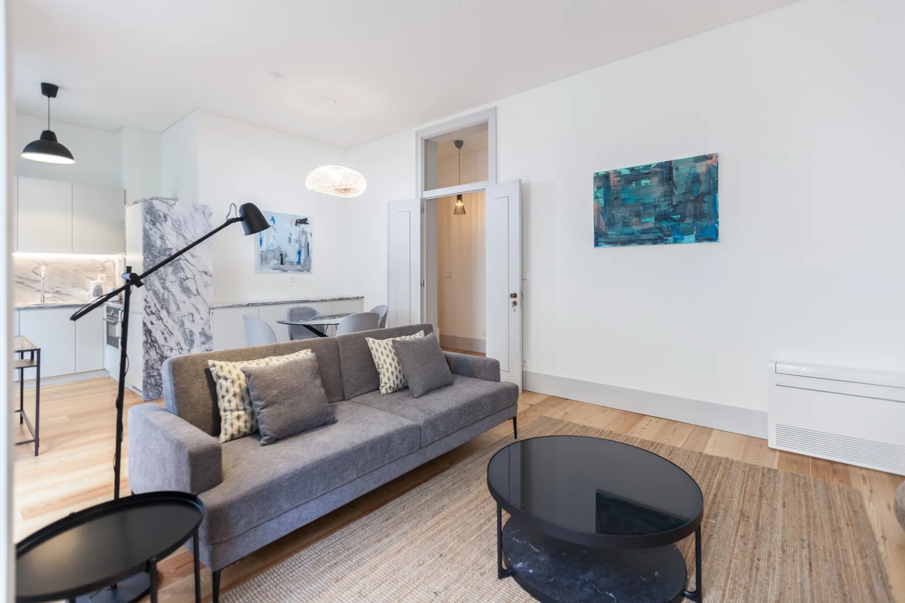 A bright living room with gray seating, a black coffee table, and an open kitchen.