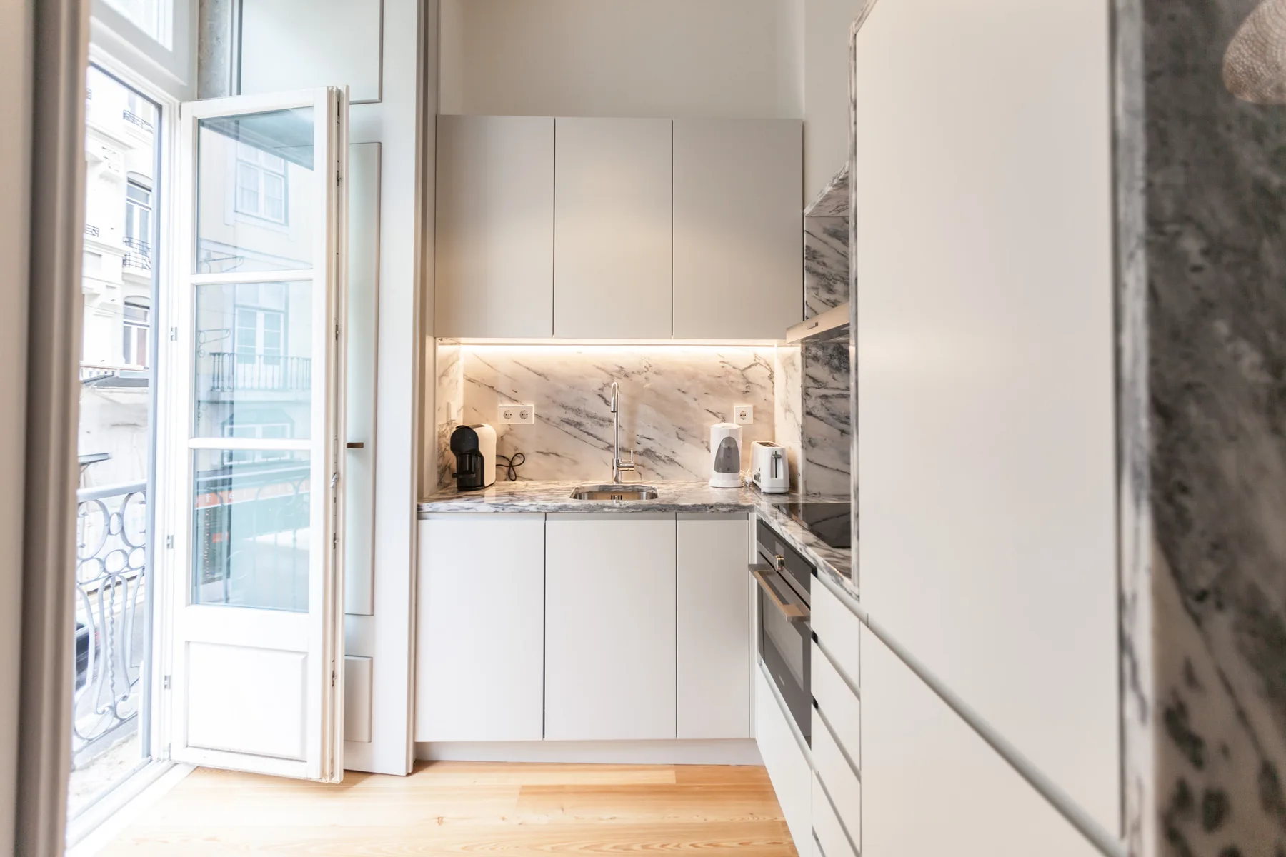 A bright modern kitchen with white cabinets and a marble backsplash.