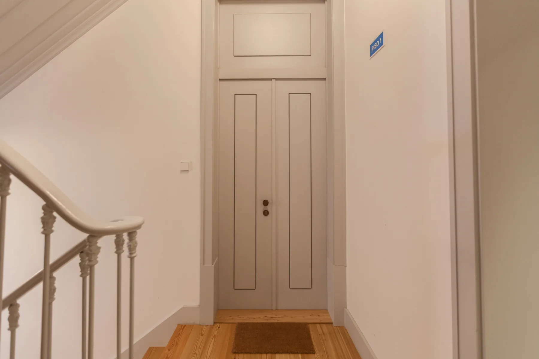 A narrow hallway ends at a paneled door, with a staircase railing along one side.