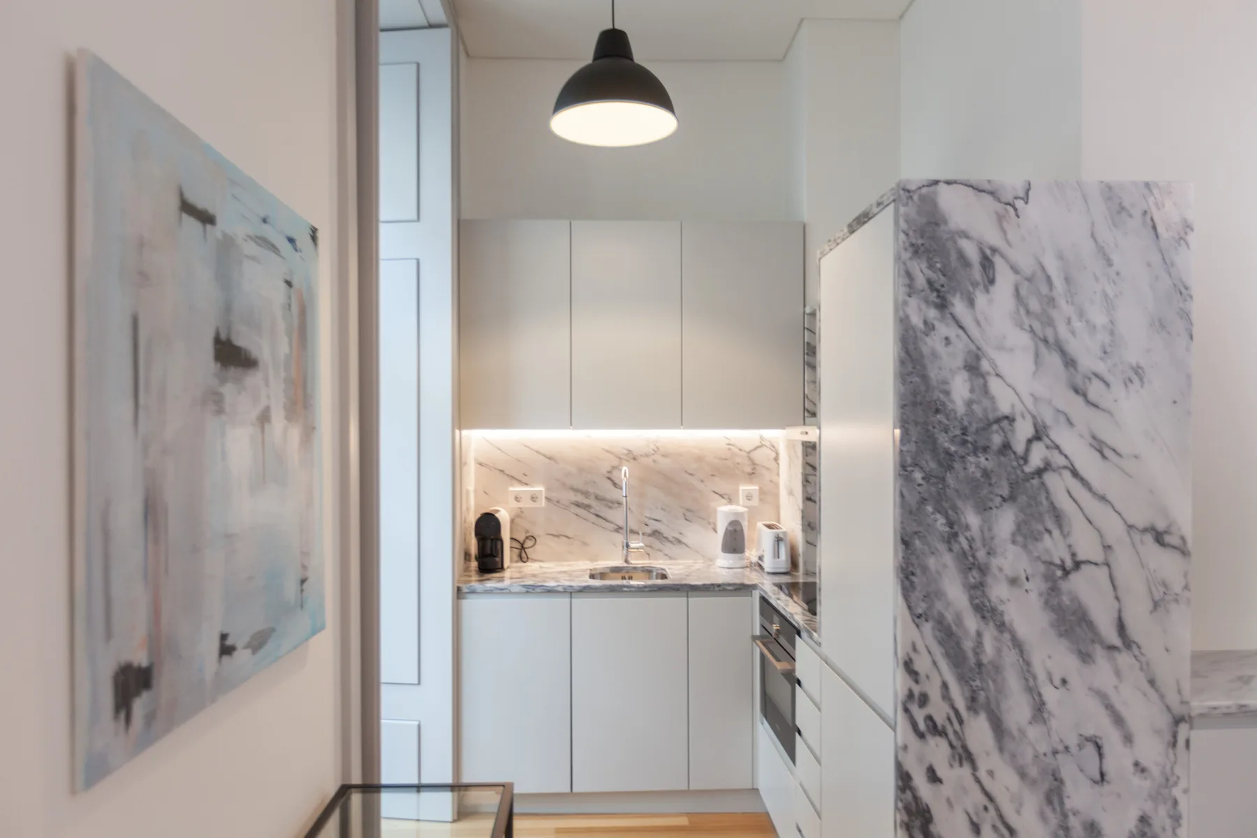 A compact kitchen with white cabinets, a cooktop, and marble-patterned surfaces.
