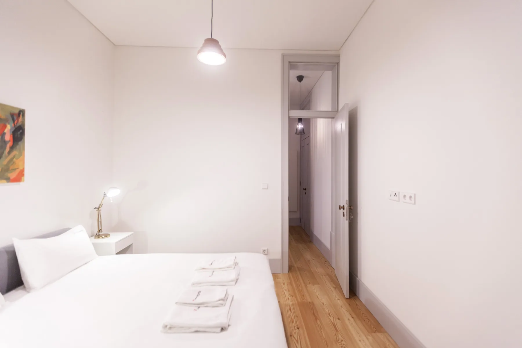 A bright bedroom with a bed, folded towels, and an open doorway.