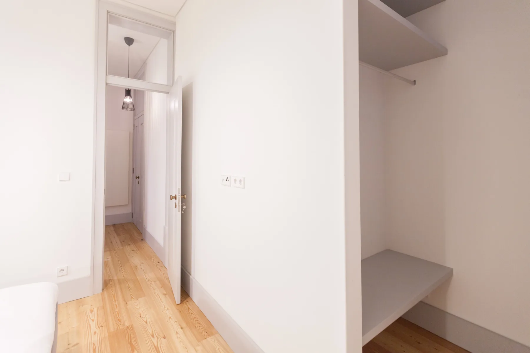 A bright apartment hallway with a wooden floor and an open closet.