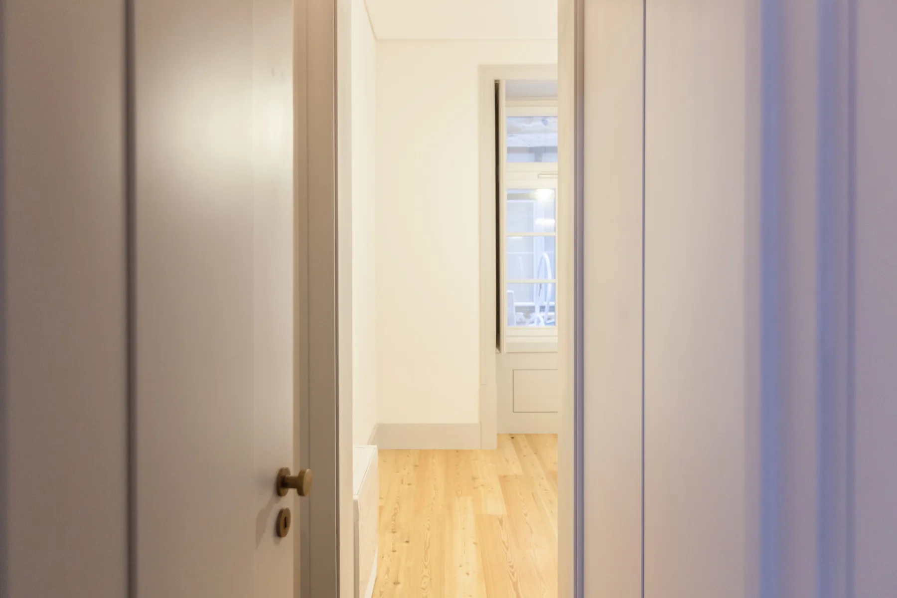 A bright hallway with light wood flooring and a window at the far end.