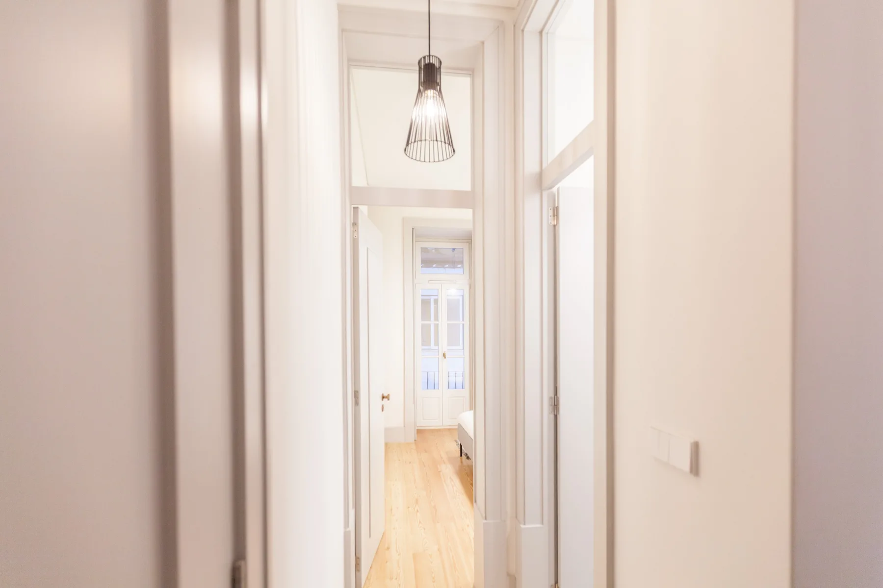A bright hallway with white walls and a pendant light.