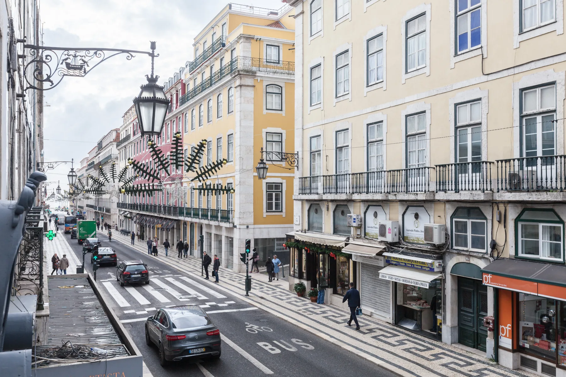 Una calle urbana bordeada de edificios de varias plantas, tiendas y coches estacionados.