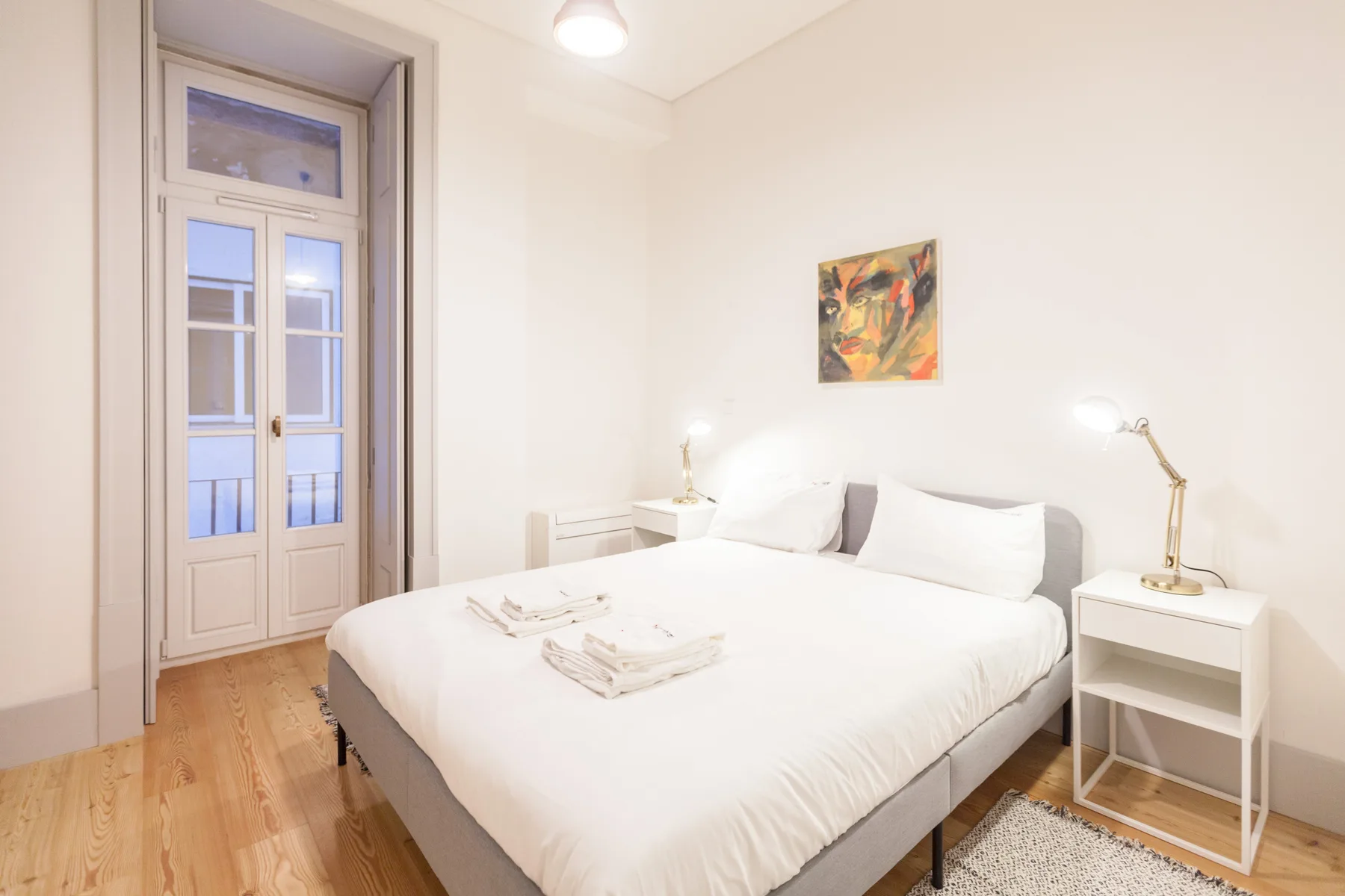 A bright bedroom with a neatly made bed and a tall window.