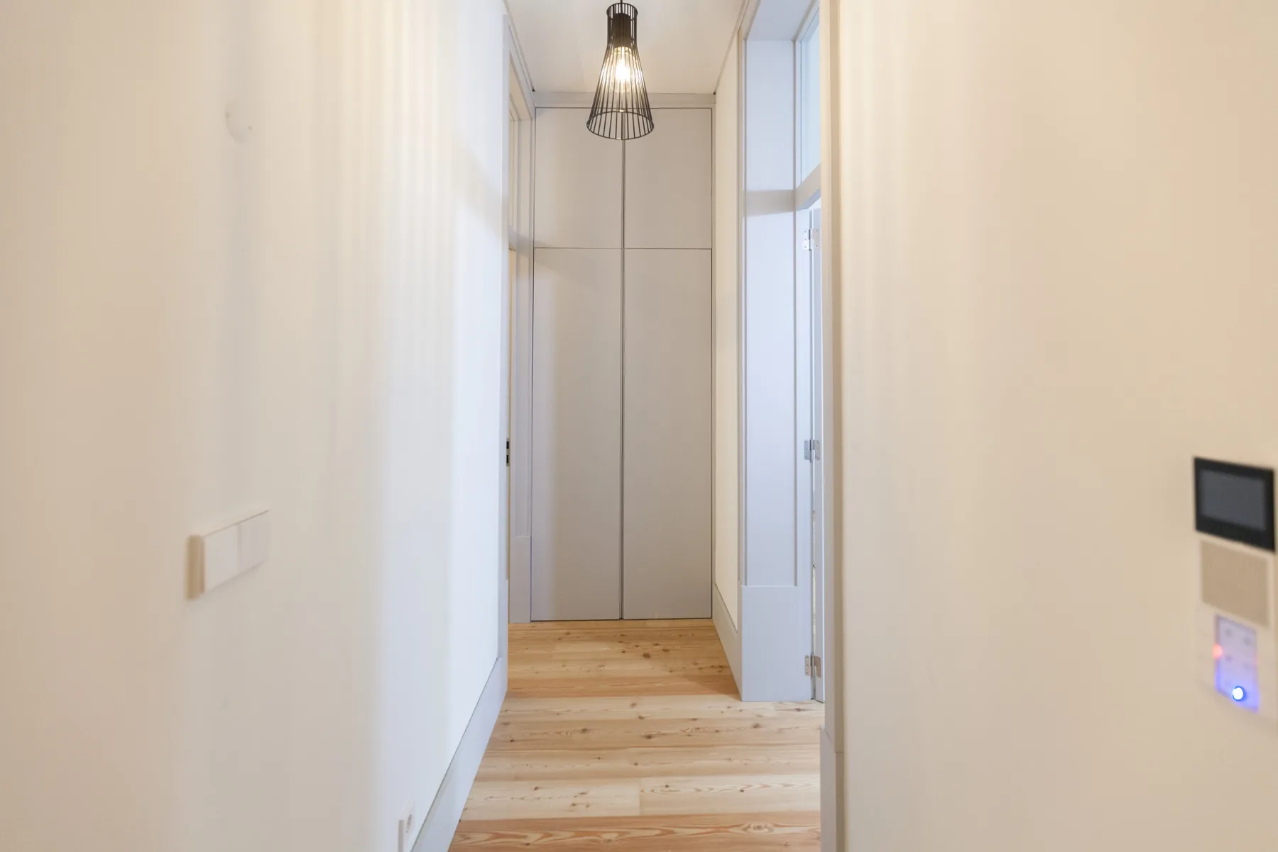 A bright hallway with light wood flooring leads to a closed door.