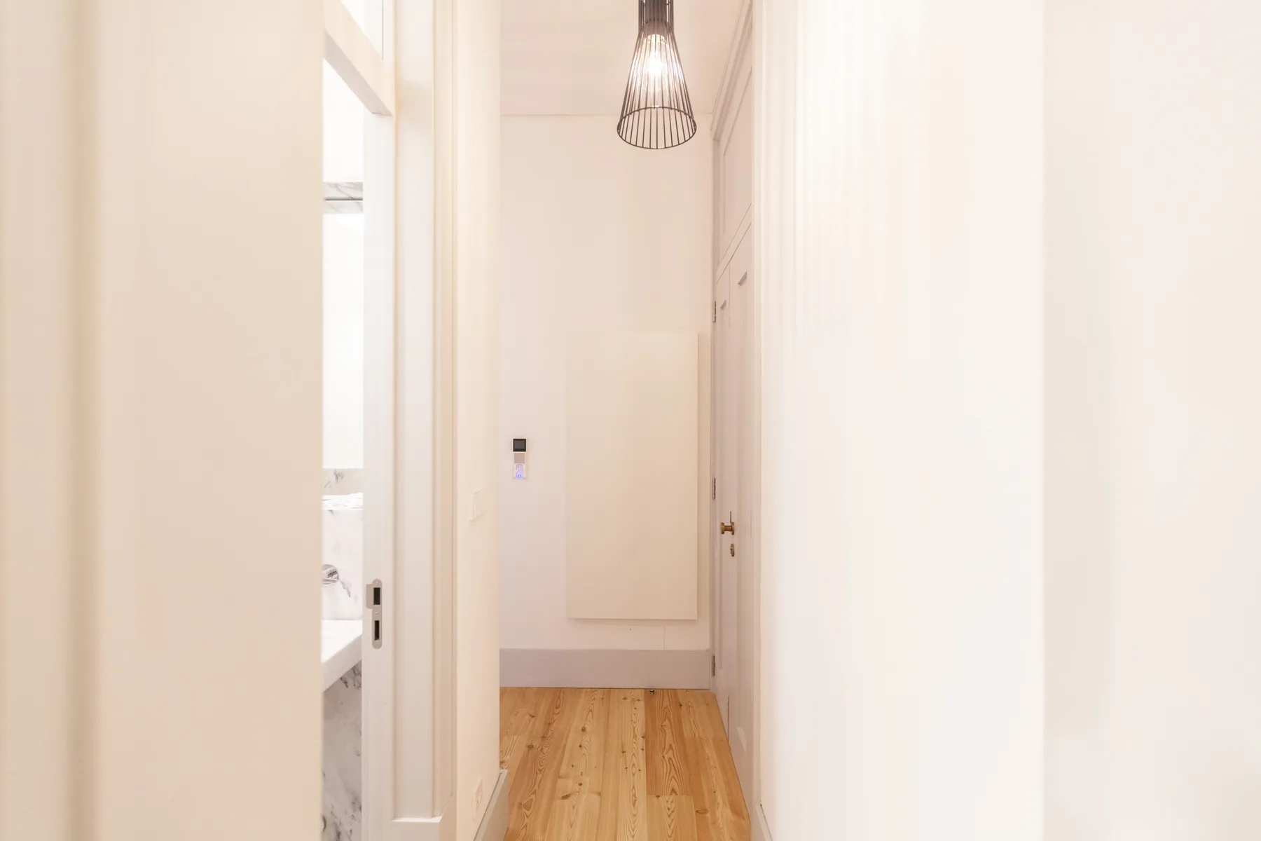 A narrow hallway with light wood flooring and a hanging pendant light.