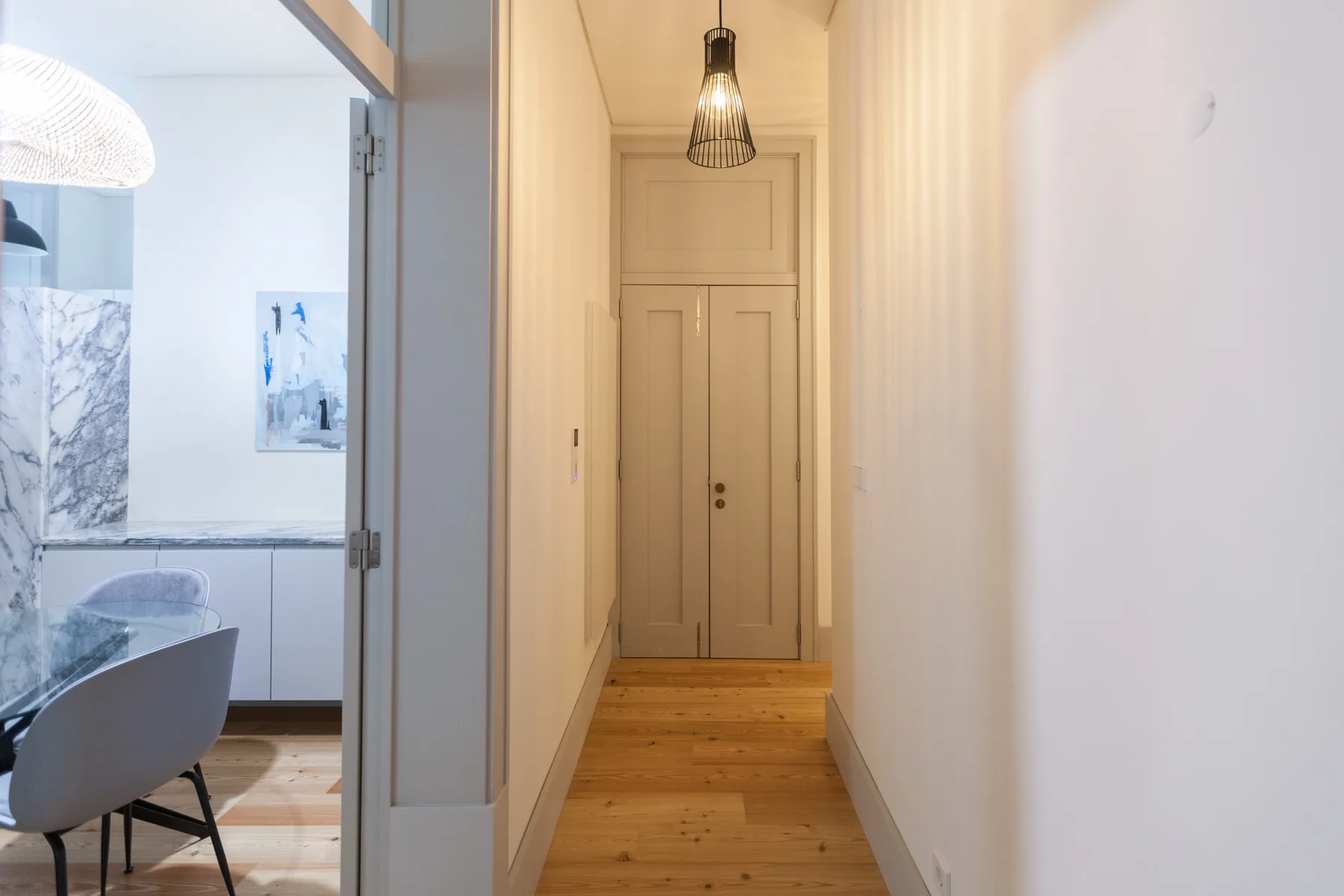 A narrow hallway with a wooden floor leads to a closed door.