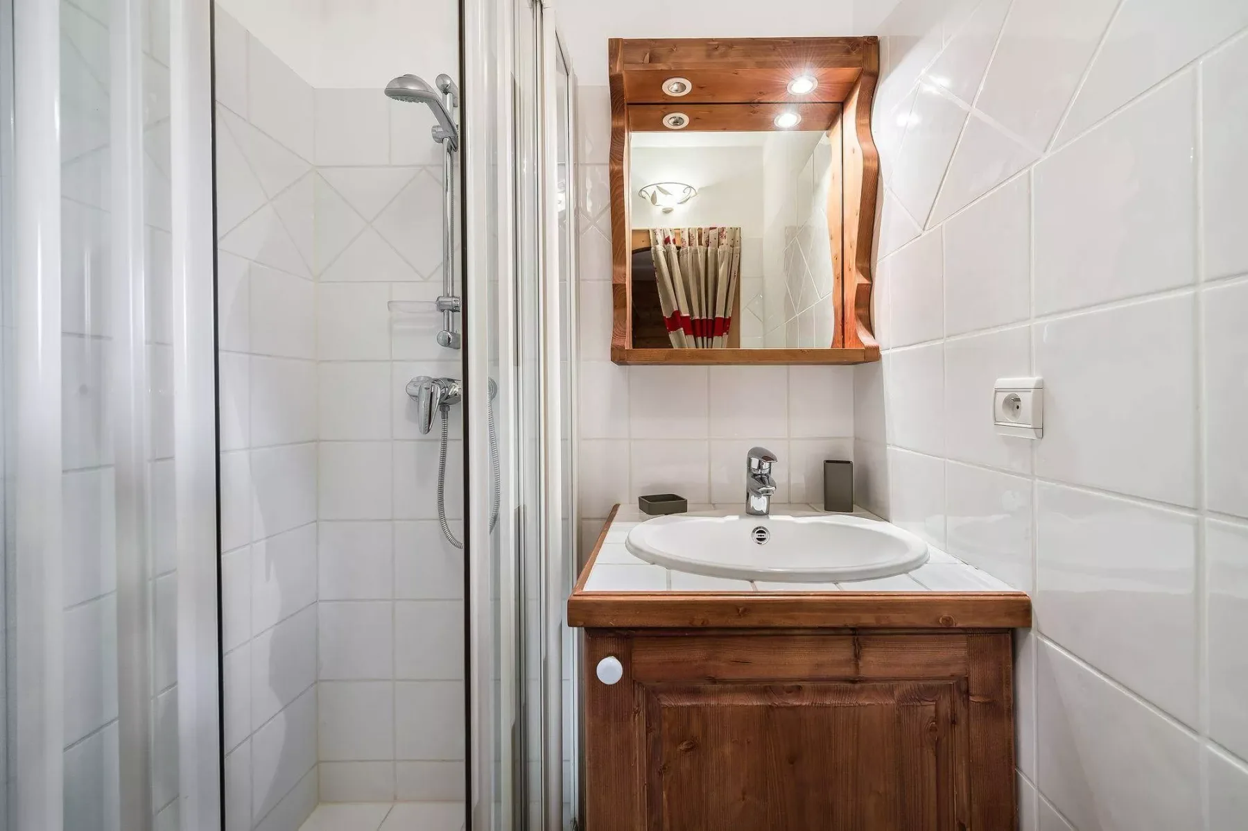 A tiled bathroom with a shower and a sink beneath a mirror.