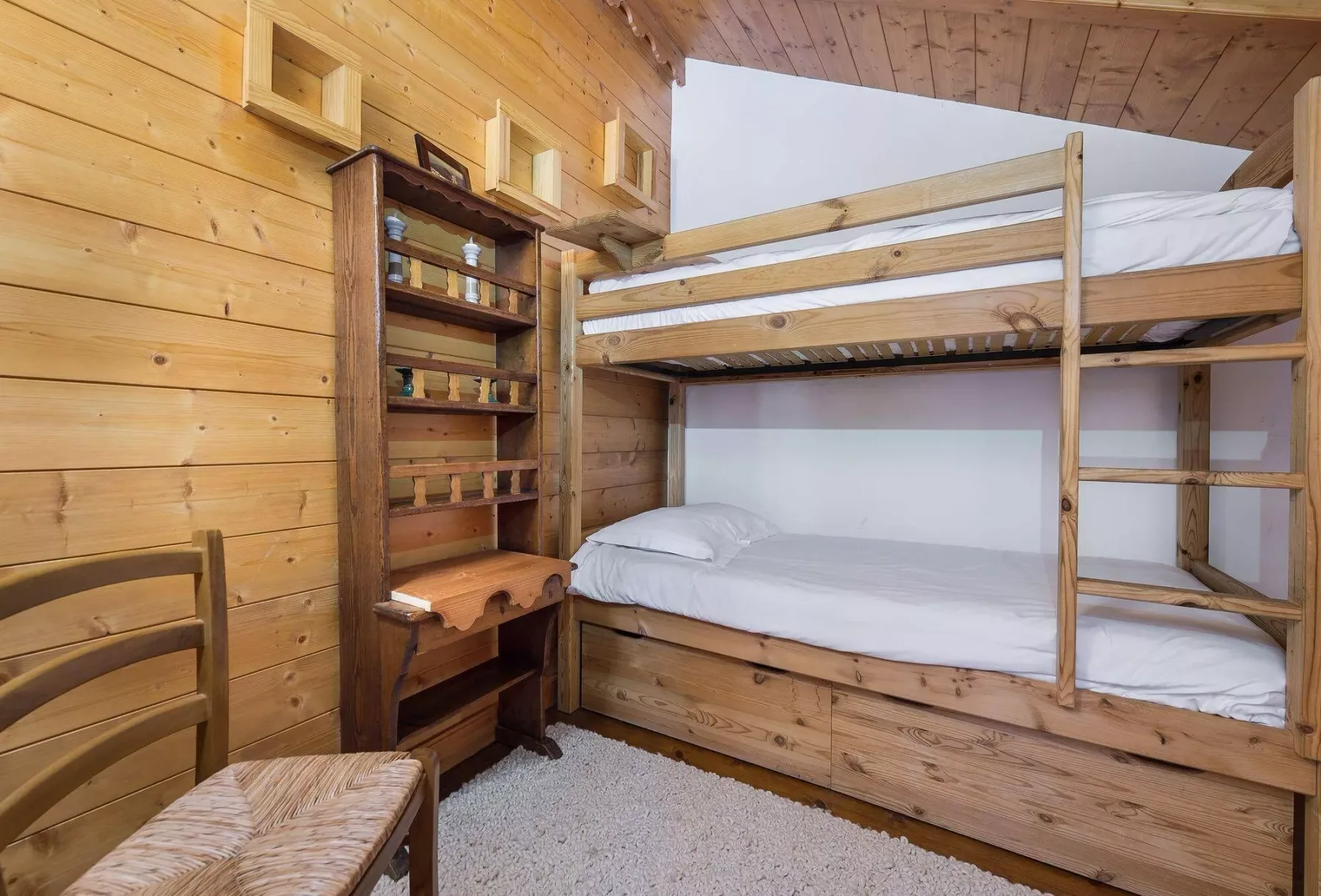 A wood-paneled bedroom with bunk beds and a narrow bookcase.